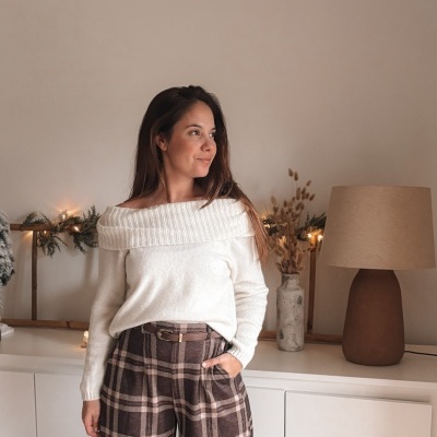 Mulher com camisola branca de malha e calças castanhas xadrez numa sala com decoração natalícia e lâmpada