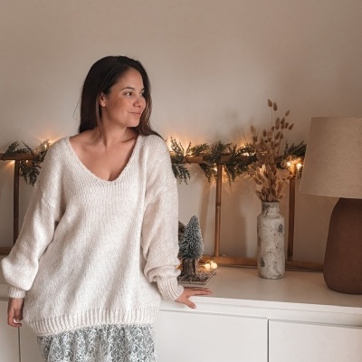 Mulher com camisola branca oversized e renda, calças pretas, junto a aparador com decoração natalícia