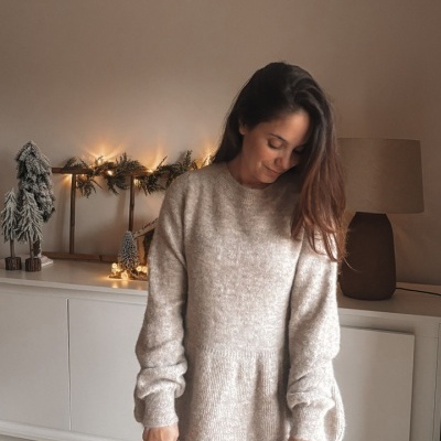 Mulher com camisola de malha castanha clara e calças de ganga azul em ambiente interior decorado para o Natal