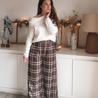 Mulher com camisola branca e calças xadrez castanhas numa sala decorada com enfeites natalícios.