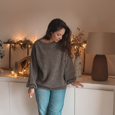 Mulher com camisola cinza e calças de ganga junto a cómoda branca e decoração natalícia