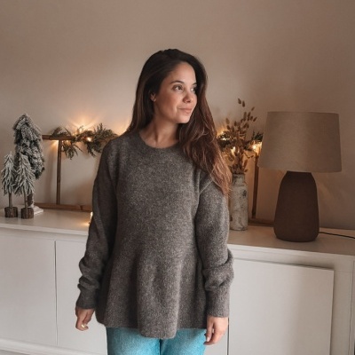 Mulher com camisola cinza escuro e calças de ganga azuis em ambiente interior com decoração natalícia.