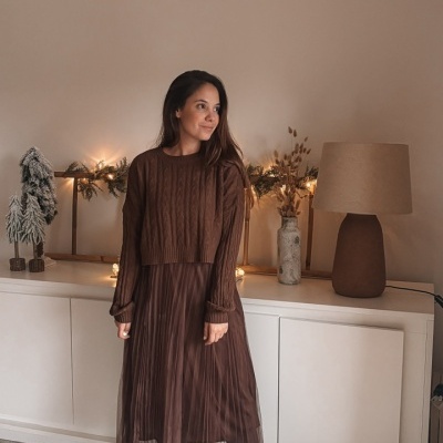 Mulher com vestido e camisola castanhos em ambiente decorado