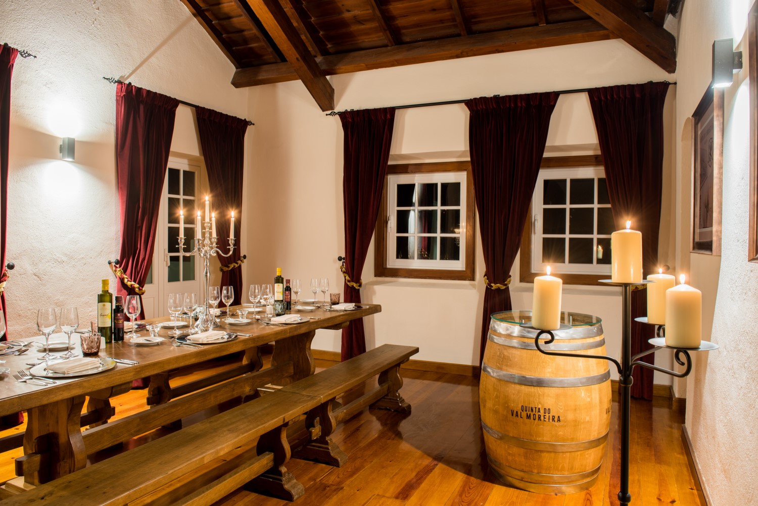 Viagem à medida Sala de jantar rústica com mesa de madeira, bancos, velas acesas, cortinas vermelhas e barril de vinho