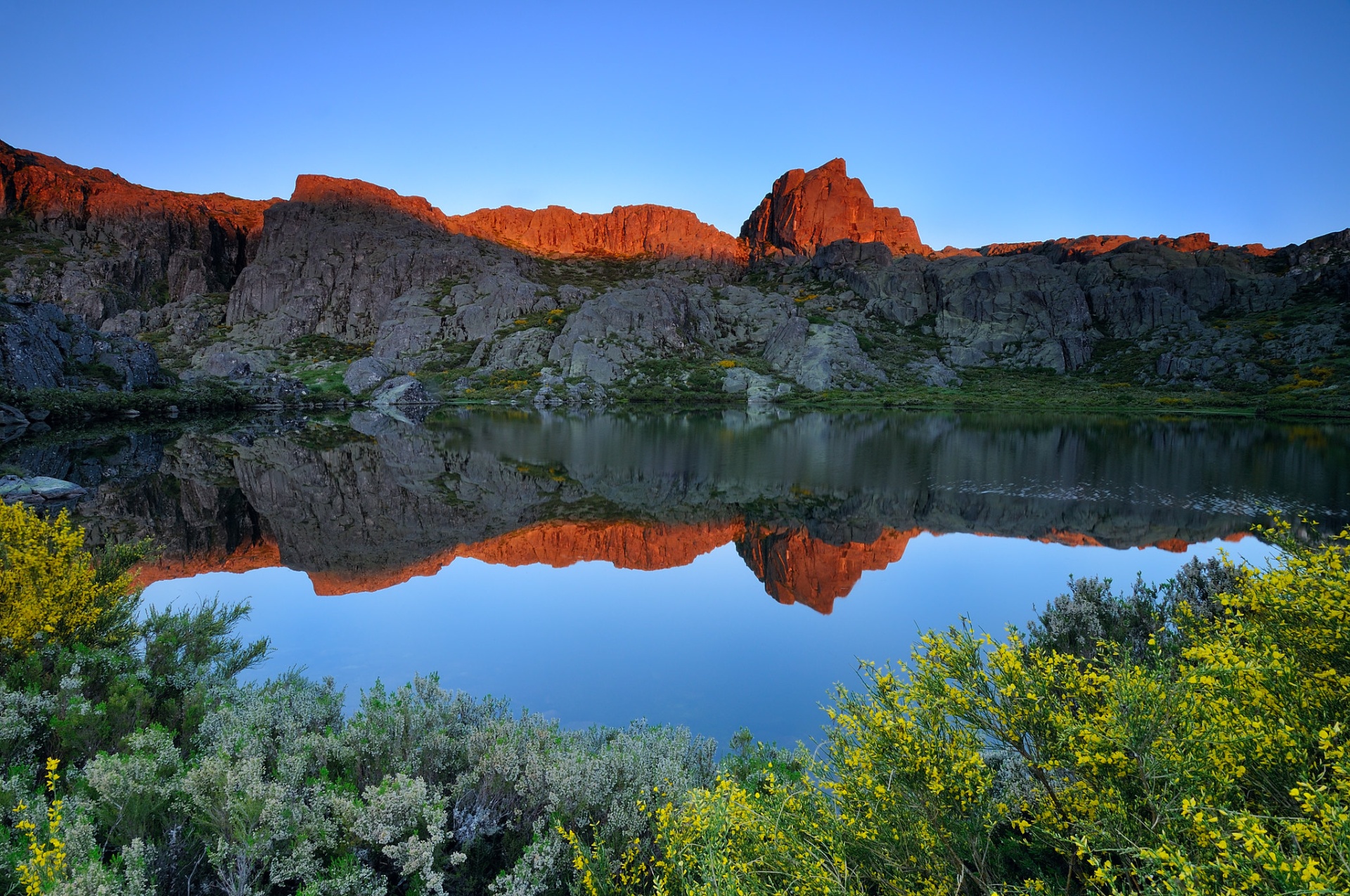 Serra da Estrela – Férias de Natureza e Tradição no Coração de Portugal Lago com montanhas rochosas refletidas e vegetação colorida em primeiro plano