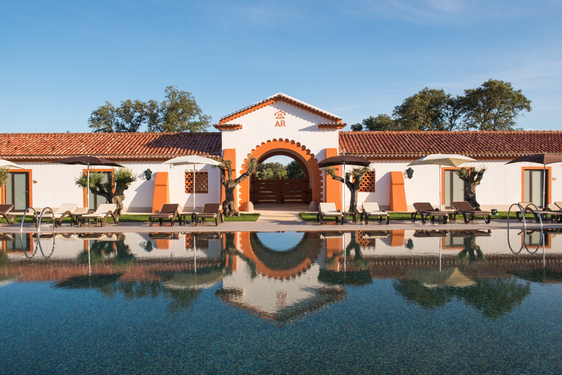 Viagem à medida Piscina exterior com edifício branco e detalhes alaranjados refletido na água