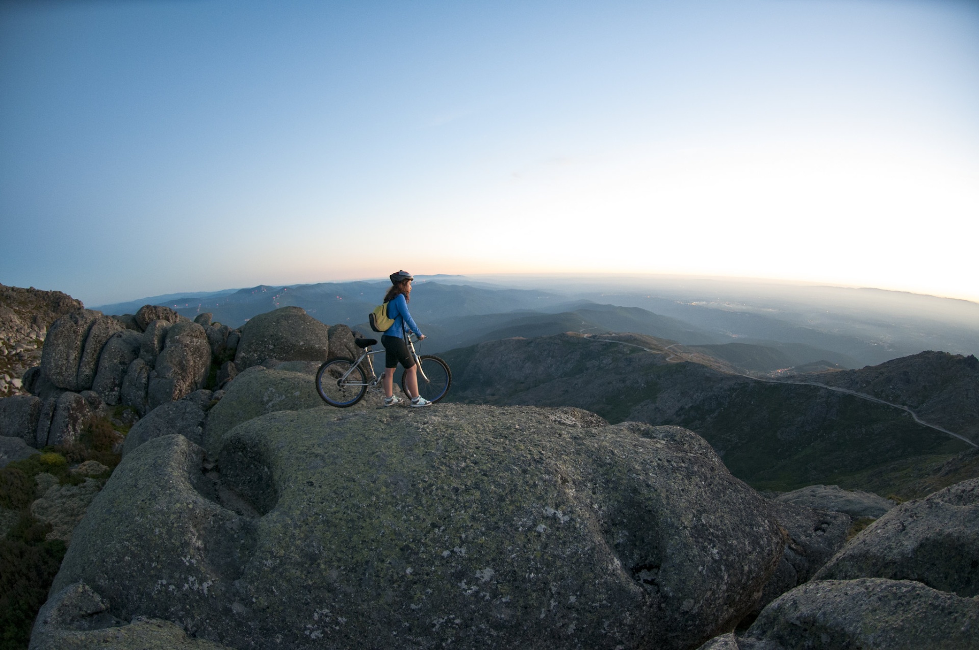 Serra da Estrela – Férias de Natureza e Tradição no Coração de Portugal Pessoa com capacete e bicicleta sobre rocha com montanhas ao fundo.