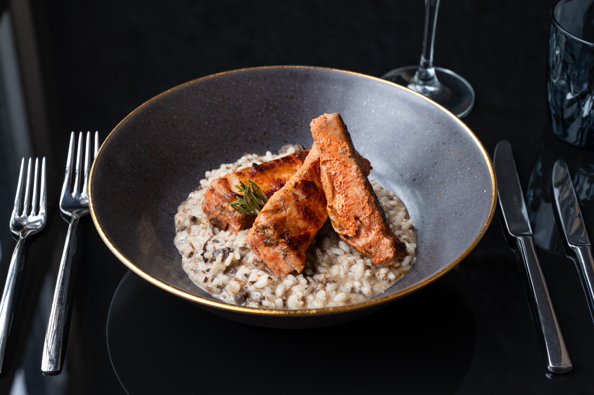 Açores – Nove Ilhas, Um Paraíso Inesquecível Prato com risoto de cogumelos e salmão grelhado sobre mesa preta com talheres e copos