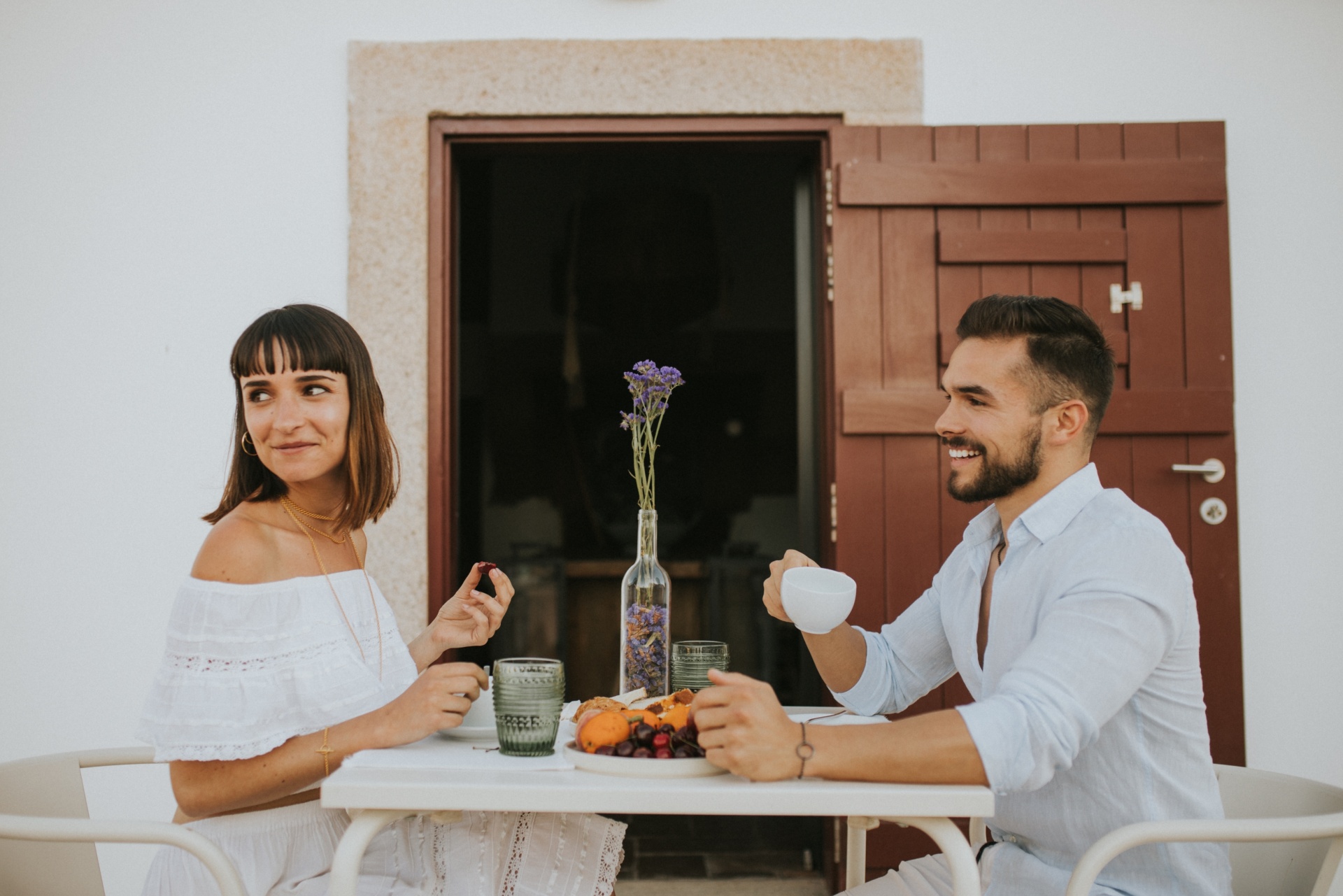Viagem à medida Casal sentado à mesa branca com fruta e flores, porta castanha ao fundo