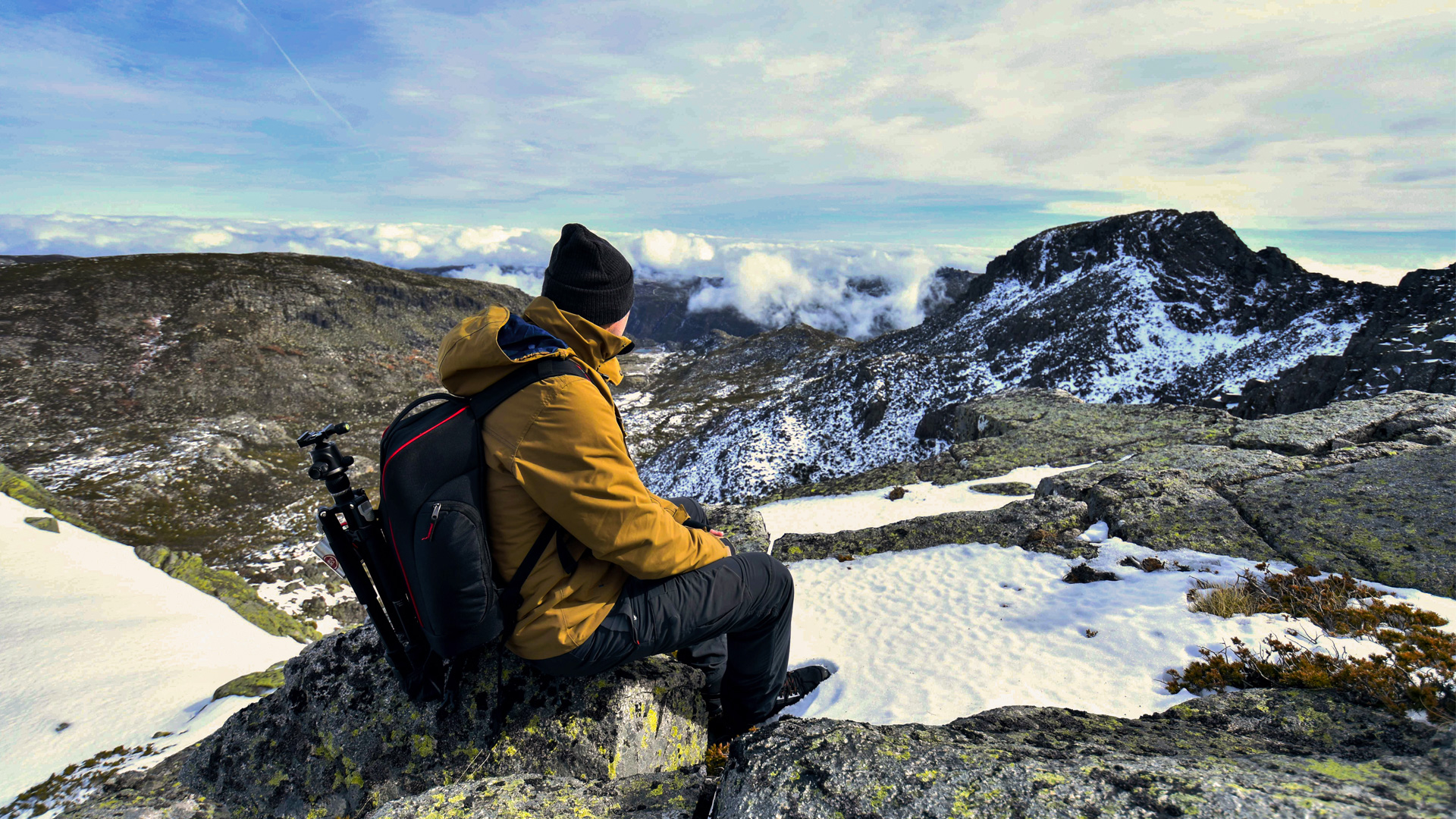 Serra da Estrela – Férias de Natureza e Tradição no Coração de Portugal Pessoa sentada em rochas com casaco amarelo e mochila na natureza montanhosa com neve.