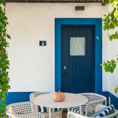 Conjunto mesa e cadeiras brancas com almofadas azuis em frente a porta azul e parede branca