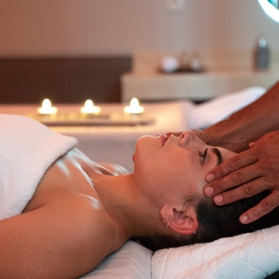 Pessoa a receber massagem na cabeça em ambiente de spa com velas