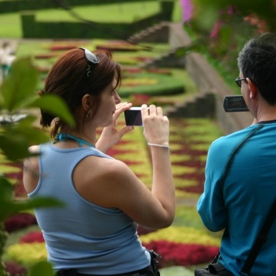 Duas pessoas a tirar fotos num jardim colorido de flores, vista de costas.