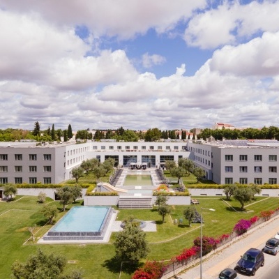Edifício moderno em forma de U com piscinas e relvado verde à volta