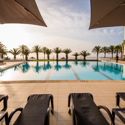 Piscina exterior com espreguiçadeiras, guarda-sóis e palmeiras em ambiente de hotel