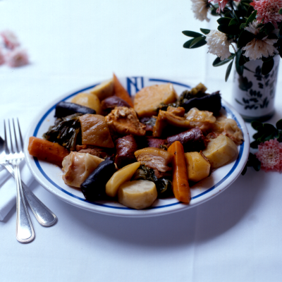 Prato com ensopado de legumes e carne ao lado de talheres e vaso com flores