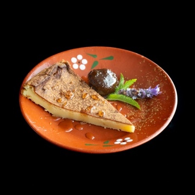 Fatia de tarte com canela e mel num prato de cerâmica com decoração floral, bola de chocolate e ramo com flor.