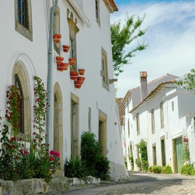 Rua estreita com casas brancas e vasos de barro vermelhos pendurados