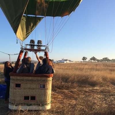 Balão de ar quente com cesto de vime e pessoas a bordo em campo seco ao pôr do sol