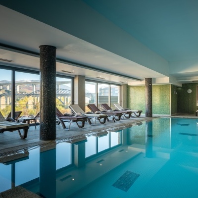 Piscina interior com cadeiras de repouso e janelas panorâmicas para paisagem exterior