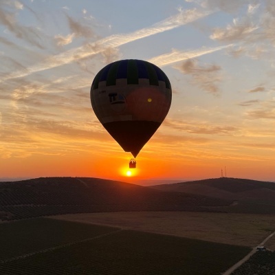 Balão de ar quente azul e verde ao pôr do sol sobre paisagem rural