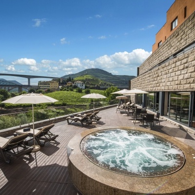 Jacuzzi exterior redondo com espreguiçadeiras e guarda-sóis numa varanda com vista montanhosa