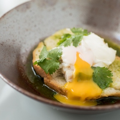 Ovo escalfado com pão e coentros numa tigela castanha