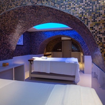 Sala de massagem com camas brancas e azulejos coloridos nas paredes e teto