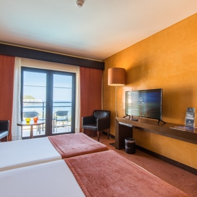 Quarto de hotel com camas, poltronas, televisão e varanda com vista para o mar