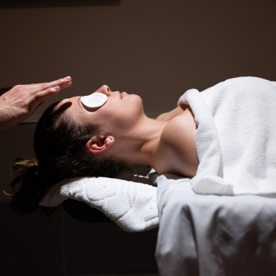 Mulher numa cama de massagem com discos de algodão nos olhos e terapeuta a aplicar tratamento no rosto