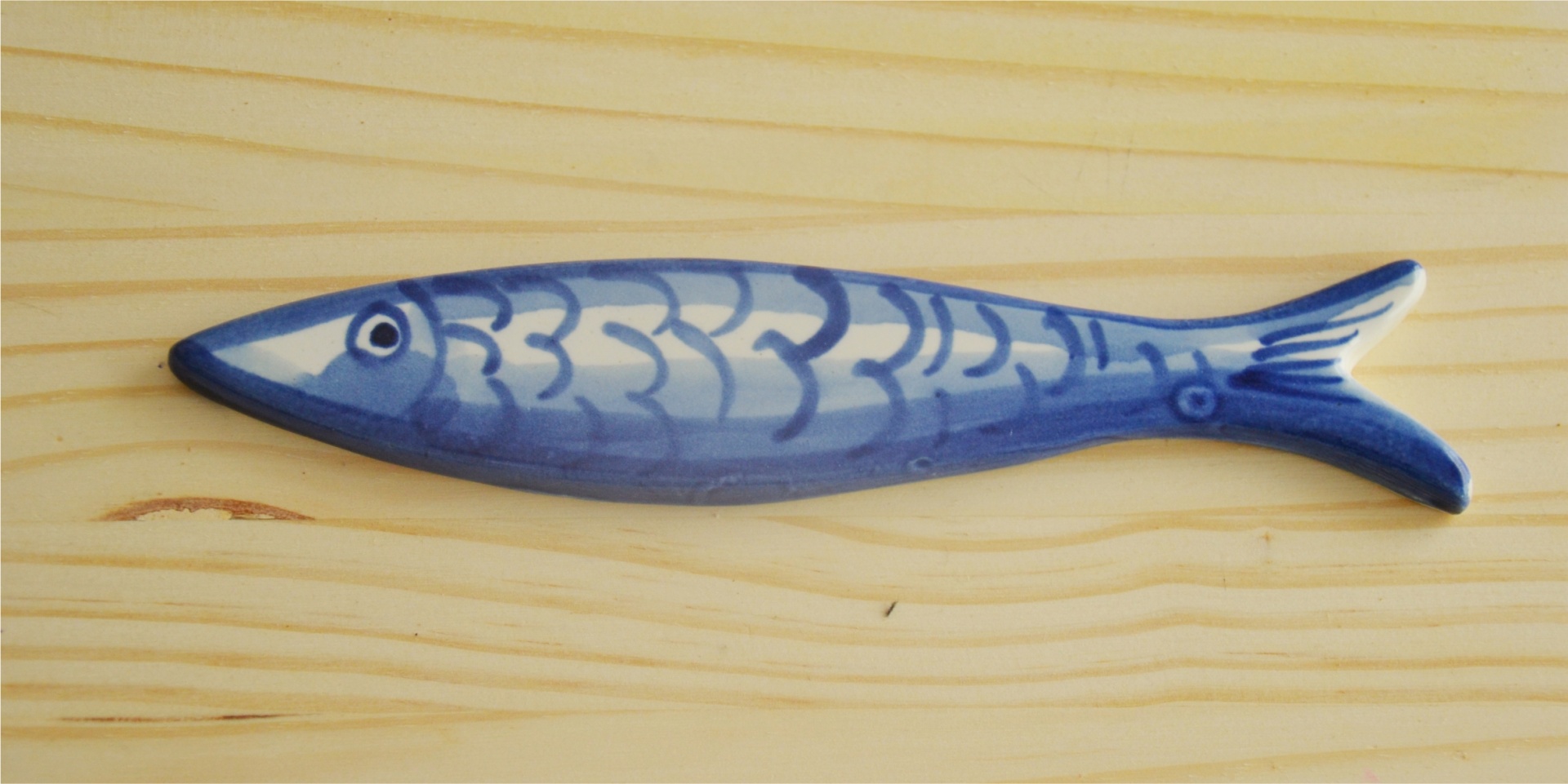 Blue and white ceramic fish-shaped object on light wooden surface