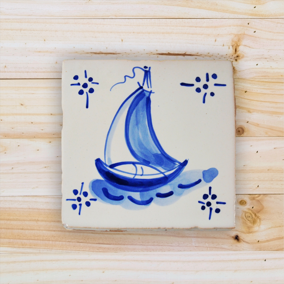 Square ceramic tile with blue sailboat design on white background
