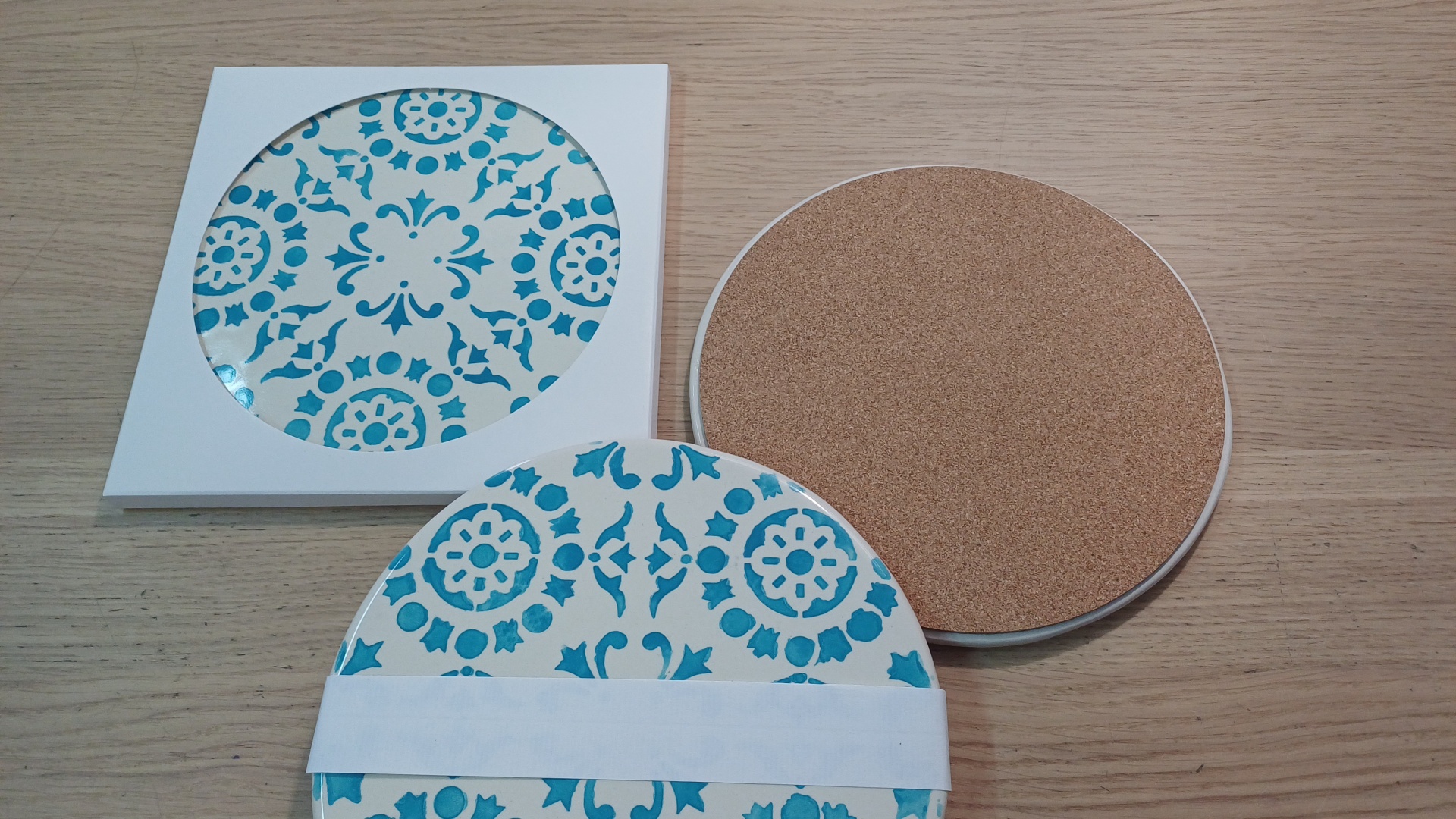 Round ceramic tile coasters with blue floral patterns and cork backs on wood surface