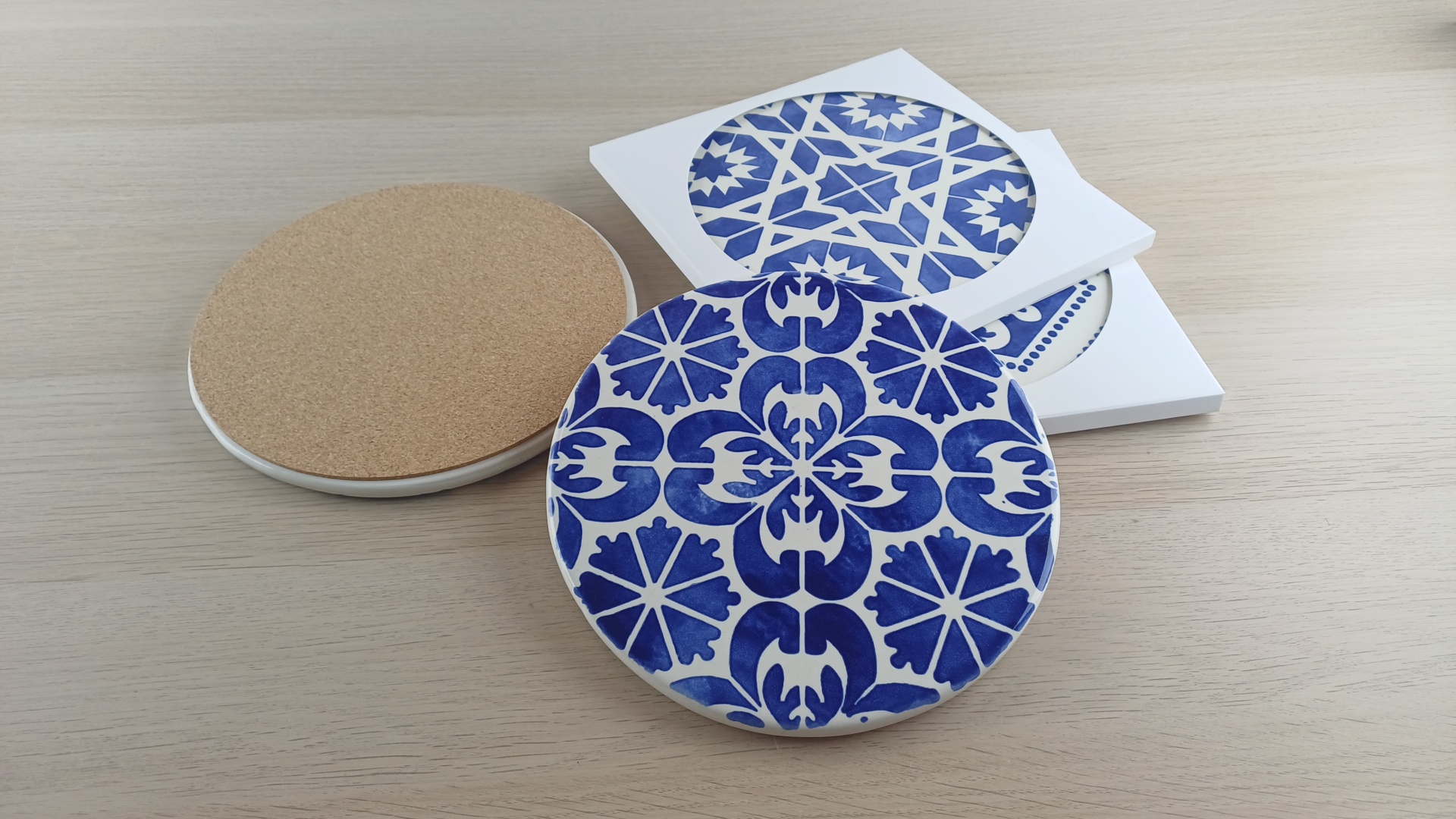 Blue and white patterned ceramic coasters with cork backing on a wooden surface and white packaging