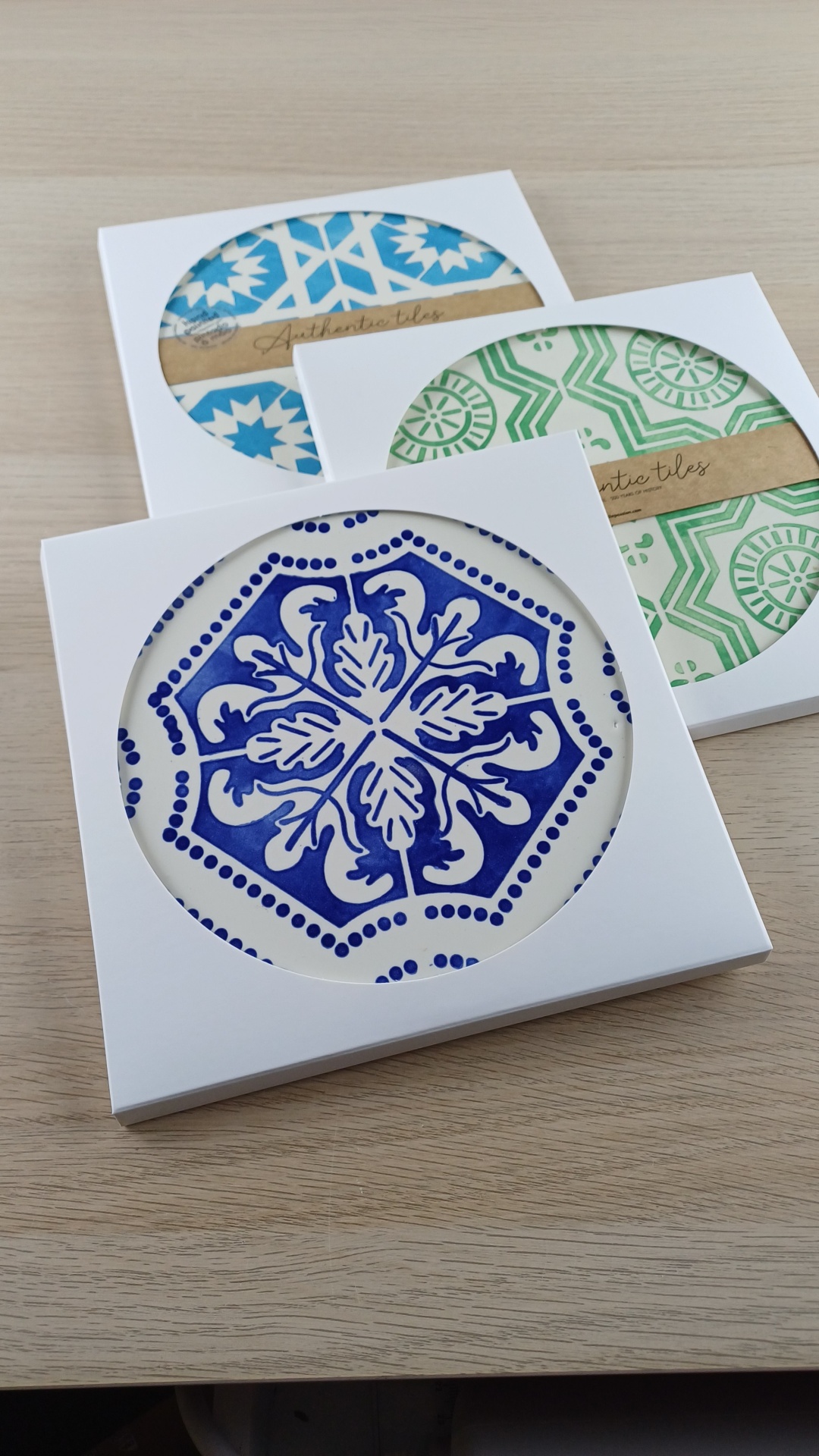Three sets of ceramic tiles in white packaging with Authentic tiles labels on a wooden table.