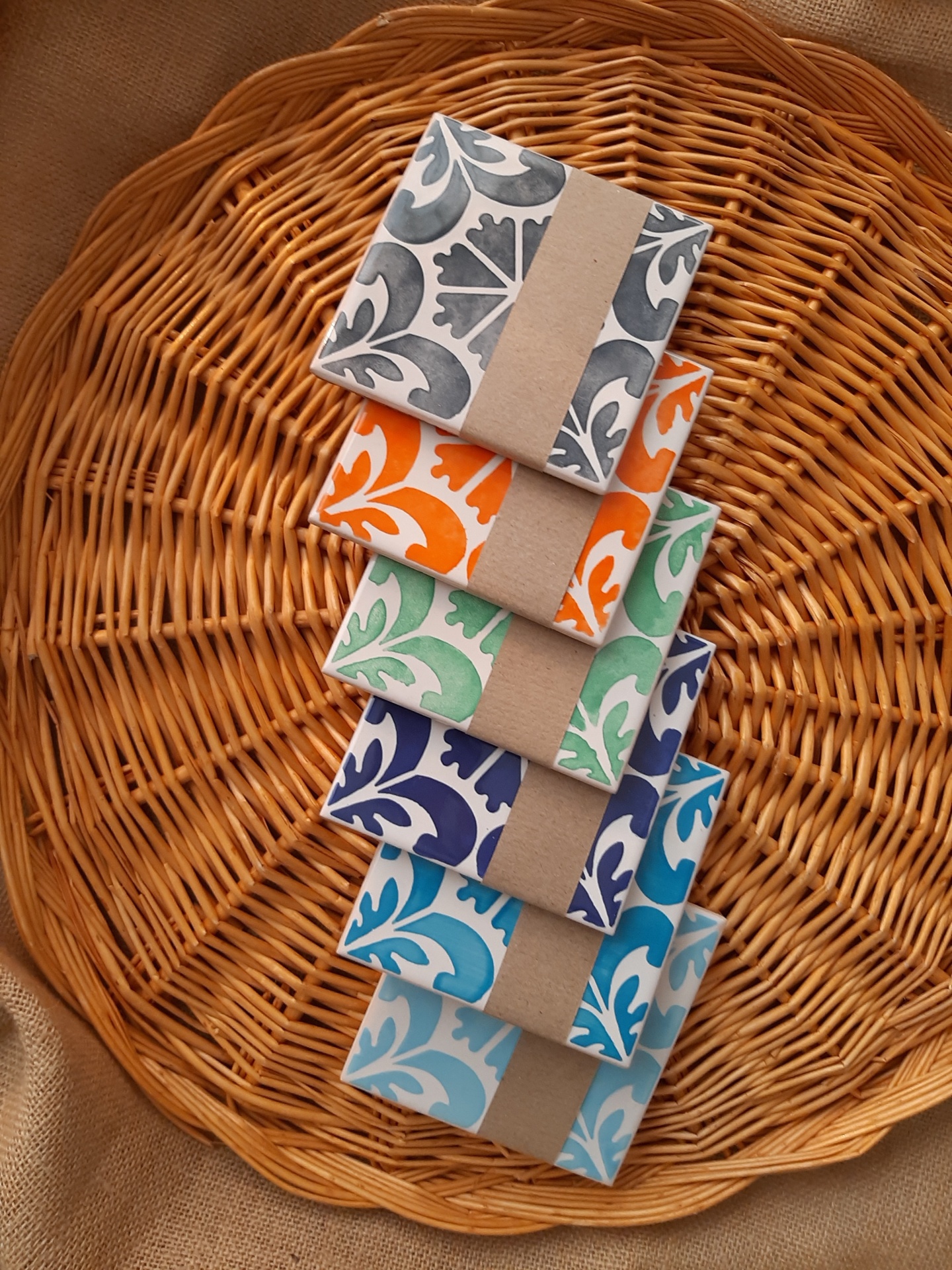 Stack of six square ceramic tiles with colorful floral patterns on a wicker tray