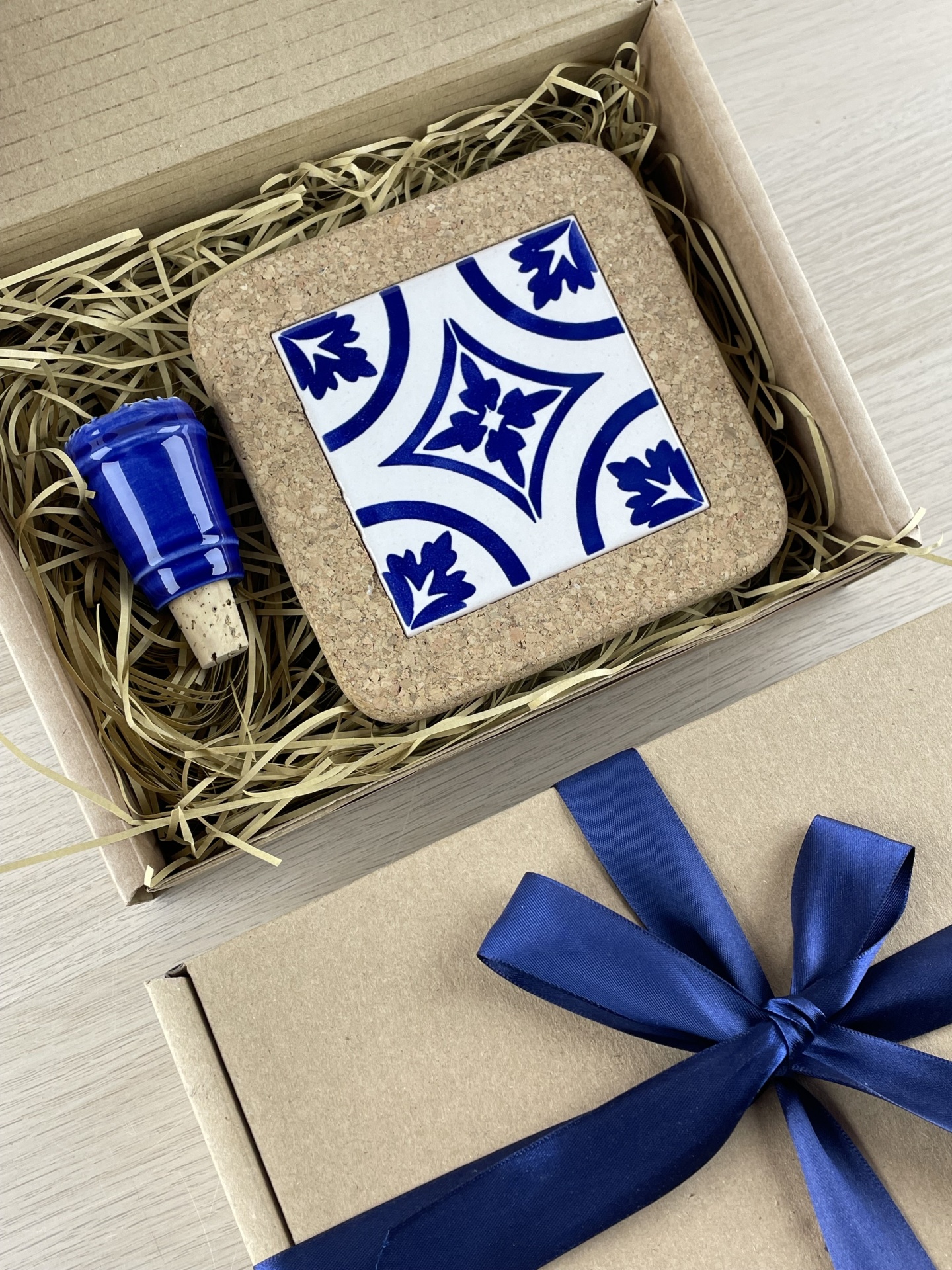 Gift box with cork coaster and blue ceramic bottle stopper in straw packing.