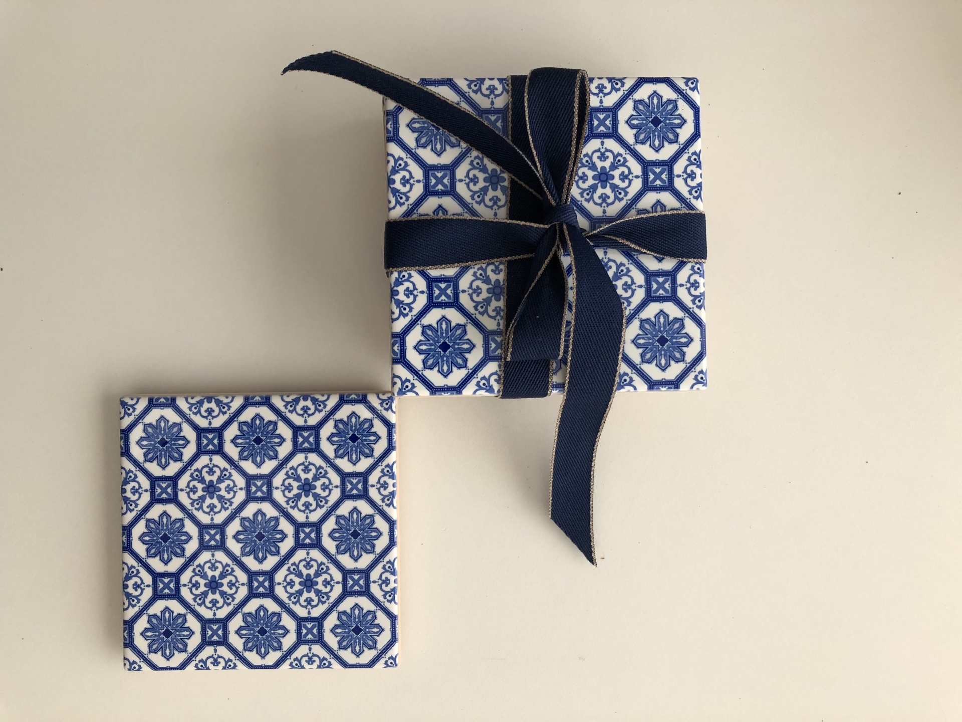 Two square tile-patterned objects, one with a dark blue ribbon bow, on a beige surface