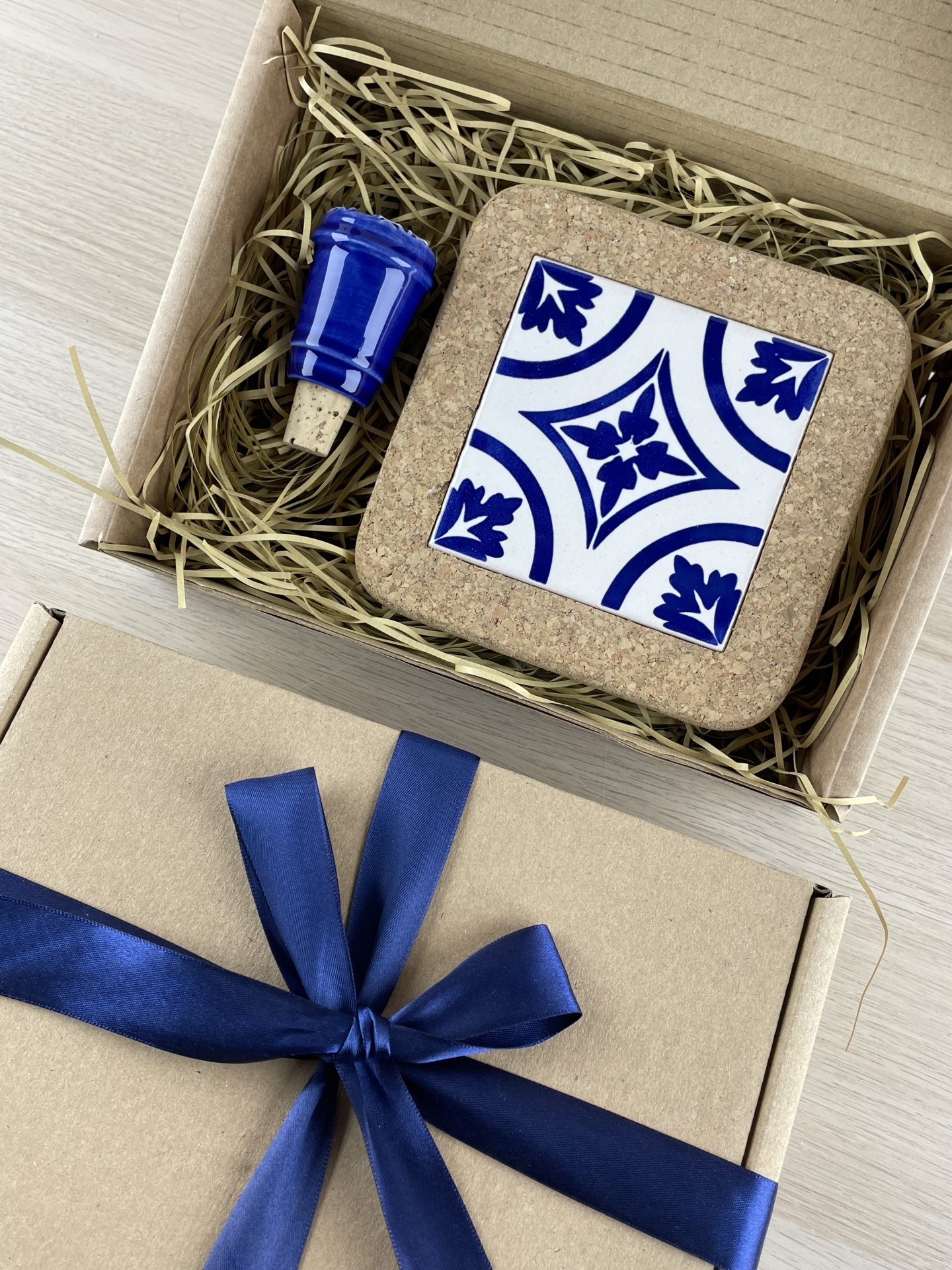 Gift set with cork coaster and bottle stopper in open box, next to a closed box with blue ribbon bow