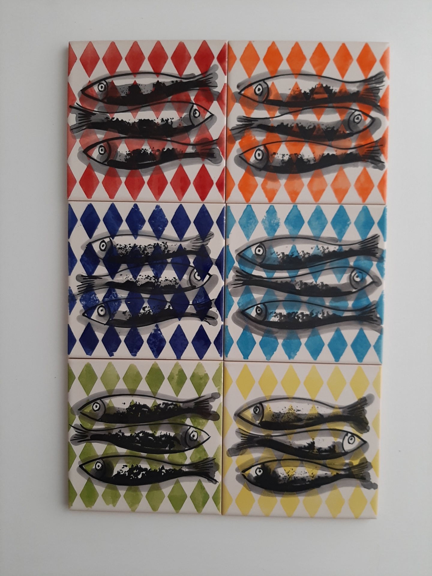 Six ceramic tiles with black fish illustrations over colorful diamond patterns in red, orange, blue, light blue, green, and yellow.