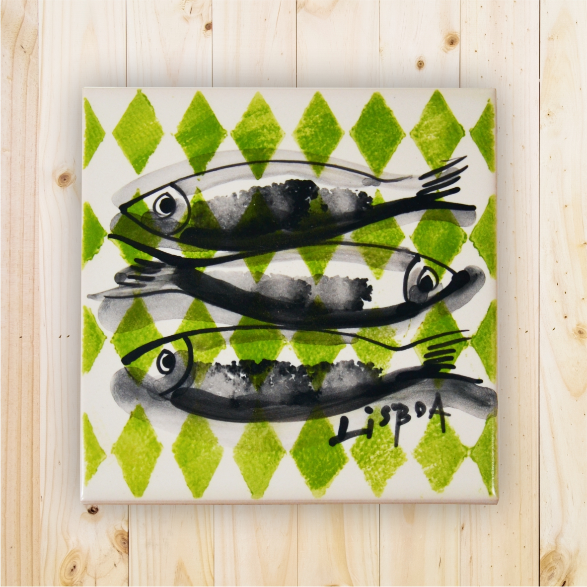 Ceramic tile with black and grey fish and green diamond pattern, signed Lisboa, on wooden surface