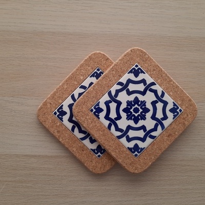 Two cork coasters with blue and white patterned ceramic centers on a wooden surface