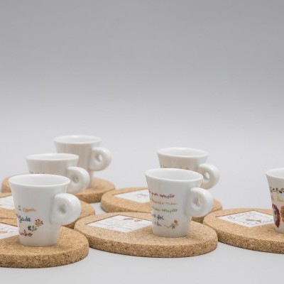 Seis chávenas de café brancas decoradas sobre suportes redondos de cortiça