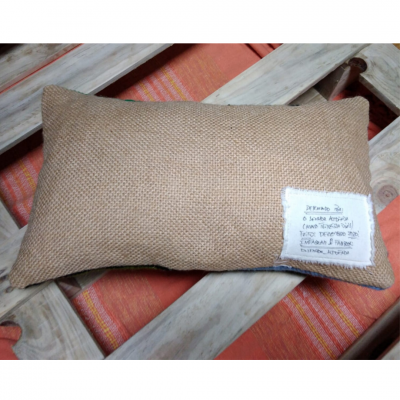 Almofada castanha com etiqueta branca sobre madeira e pano laranja às riscas