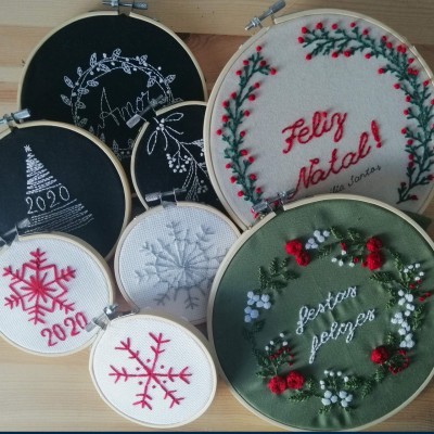 Conjunto de bordados natalícios em armações de madeira com diferentes cores e textos em português e espanhol.
