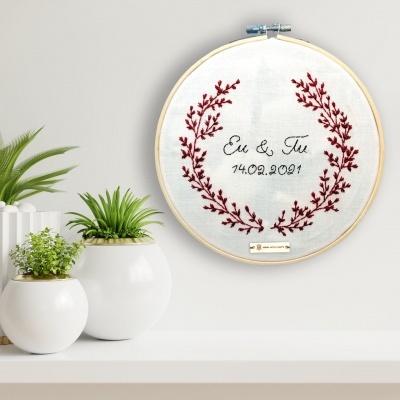 Bastidor de madeira com bordado 'Eu & Tu 14.02.2001' e plantas em vasos brancos.