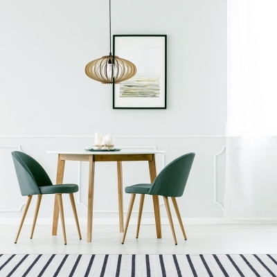 Mesa de jantar branca e madeira com duas cadeiras verdes e tapete listrado