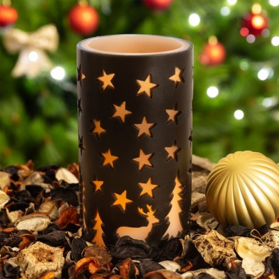 Porta-vela cerâmico preto com recortes de estrelas e cervos iluminado, sobre pot-pourri, com bola dourada e árvore de Natal ao fundo