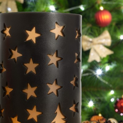 Lanterna preta com recortes de estrelas iluminada em frente a árvore de Natal decorada.