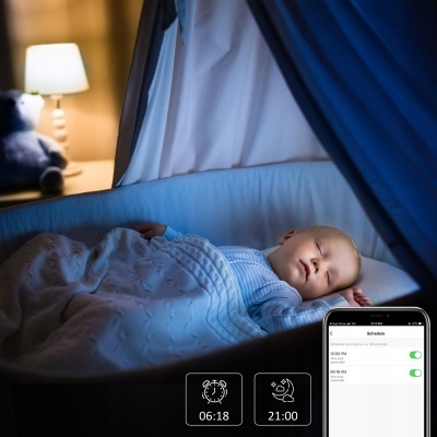 Bebé a dormir num berço azul com cobertor branco e telemóvel com horários na imagem